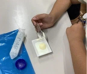 子供がスプーンで小さな白い容器に入った黄色い物体をすくっている場面です。