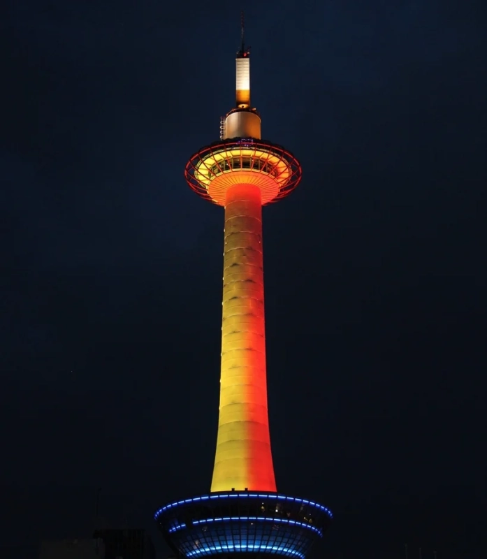 夜空にそびえ立つ京都タワーが、赤、黄、青の鮮やかな光でライトアップされている様子