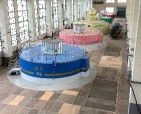 発電所の内部で、青、ピンク、黄緑色の大型発電機が3台並んでいます。